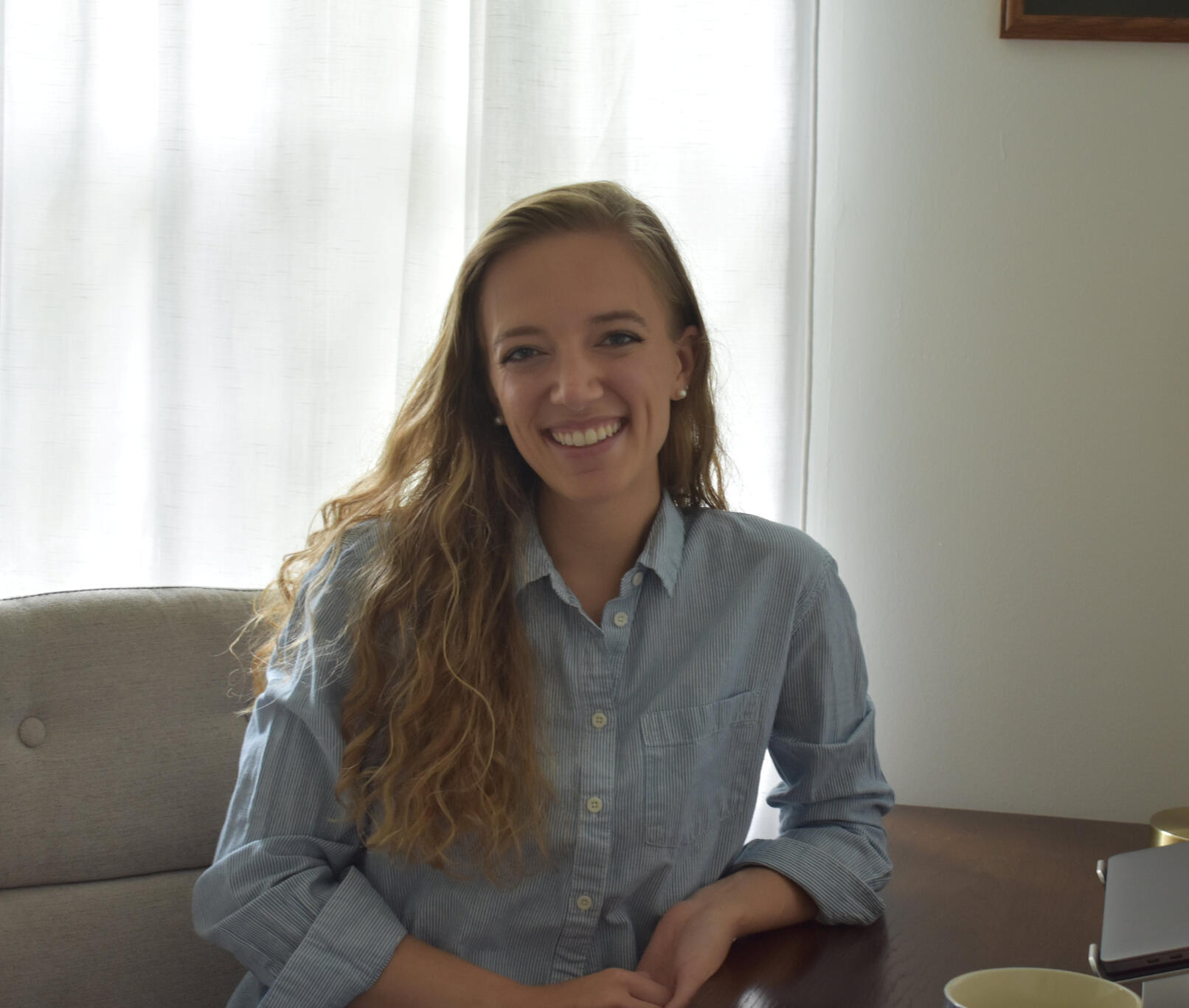 Rachel sits at a desk wearing a blue collared shirt.